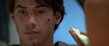 Movie still from “Point Break” (1991), directed by Kathryn Bigelow – A person with a knife on his face; Close Up shot, Low angle