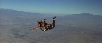 Movie still from “Point Break” (1991), directed by Kathryn Bigelow – A person is in the air while parachuting; Wide shot, Overhead angle