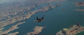 Movie still from “Point Break” (1991), directed by Kathryn Bigelow – A man is in the air with a parachute over a body of water; Wide shot, Overhead angle