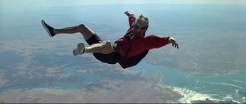 Movie still from “Point Break” (1991), directed by Kathryn Bigelow – A man is in the air with a parachute; Wide shot, Overhead angle