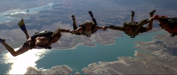 Movie still from “Point Break” (1991), directed by Kathryn Bigelow – A group of parachutists are flying over a body of water; Wide shot, Overhead angle