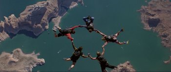 Movie still from “Point Break” (1991), directed by Kathryn Bigelow – A group of skydivers are in the air with their arms in the air; Extreme Wide shot, Overhead angle