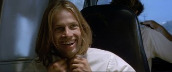 Movie still from “Point Break” (1991), directed by Kathryn Bigelow – A man with long hair smiles while holding his tie; Close Up shot, Low angle