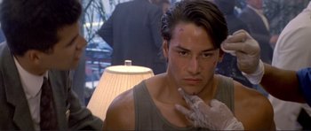 Movie still from “Point Break” (1991), directed by Kathryn Bigelow – A person sitting in front of a lamp; Close Up shot, Over the shoulder angle