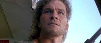 Movie still from “Point Break” (1991), directed by Kathryn Bigelow – A man with long hair and blue eyes; Close Up shot, Low angle