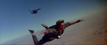 Movie still from “Point Break” (1991), directed by Kathryn Bigelow – Two people are parachuted into the sky; Wide shot, Low angle
