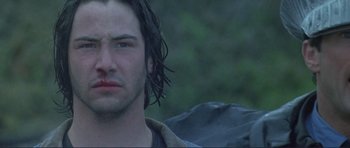 Movie still from “Point Break” (1991), directed by Kathryn Bigelow – A man with long hair and a bruised face; Close Up shot, Low angle