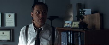 Movie still from “Pokémon: Detective Pikachu” (2019), directed by Rob Letterman – A man wearing a tie sitting in front of a desk; Medium shot, Over the shoulder angle