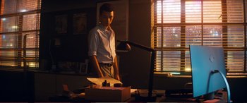 Movie still from “Pokémon: Detective Pikachu” (2019), directed by Rob Letterman – A man standing at a desk in a dimly - lit room; Medium shot, Low angle