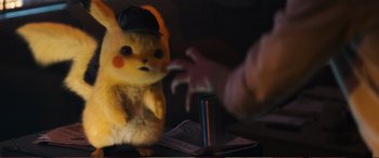 Movie still from “Pokémon: Detective Pikachu” (2019), directed by Rob Letterman – A stuffed animal wearing a black hat and holding a cell phone in front of it; Medium shot, Over the shoulder angle