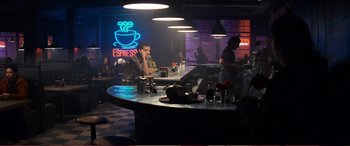 Movie still from “Pokémon: Detective Pikachu” (2019), directed by Rob Letterman – A man sitting at a counter in front of a neon sign; Wide shot, High angle