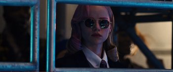 Movie still from “Pokémon: Detective Pikachu” (2019), directed by Rob Letterman – A woman with pink hair wearing sunglasses and a suit and tie; Close Up shot, Over the shoulder angle