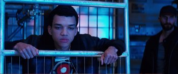 Movie still from “Pokémon: Detective Pikachu” (2019), directed by Rob Letterman – A young man leaning against a metal fence; Close Up shot, High angle