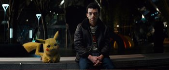 Movie still from “Pokémon: Detective Pikachu” (2019), directed by Rob Letterman – A man sitting next to a stuffed pikachu toy; Medium shot, Over the shoulder angle