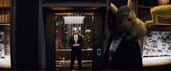 Movie still from “Pokémon: Detective Pikachu” (2019), directed by Rob Letterman – A man in a suit and tie standing in front of a window; Wide shot, Over the shoulder angle