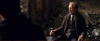 Movie still from “Pokémon: Detective Pikachu” (2019), directed by Rob Letterman – An older man sitting on the ground holding a cell phone; Medium shot, Over the shoulder angle