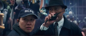 Movie still from “Pokémon: Detective Pikachu” (2019), directed by Rob Letterman – Two men in suits and hats are talking on a walkie - talkie; Close Up shot, Over the shoulder angle