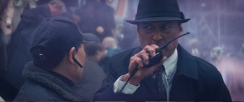 Movie still from “Pokémon: Detective Pikachu” (2019), directed by Rob Letterman – A man wearing a hat and holding two walkie talkies; Close Up shot, Over the shoulder angle