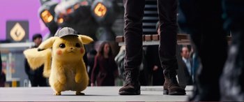 Movie still from “Pokémon: Detective Pikachu” (2019), directed by Rob Letterman – A person standing next to a person wearing a hat and shoes; Medium shot, Over the shoulder angle
