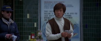 Movie still from “First Strike” (1996), directed by Stanley Tong – A man standing in front of a wall holding a stack of money; Medium shot, Over the shoulder angle