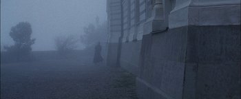 Movie still from “First Strike” (1996), directed by Stanley Tong – A person walking on a path near a building in the fog; Extreme Wide shot, Low angle