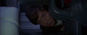 Movie still from “First Strike” (1996), directed by Stanley Tong – A young man looking at the camera from underneath a car; Close Up shot, Overhead angle