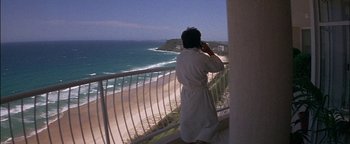 Movie still from “First Strike” (1996), directed by Stanley Tong – A woman in a robe standing on a balcony looking at the ocean; Wide shot, High angle