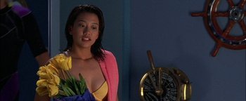 Movie still from “First Strike” (1996), directed by Stanley Tong – A woman in a yellow and pink bathing suit holding a plant; Close Up shot, High angle