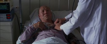 Movie still from “First Strike” (1996), directed by Stanley Tong – An older man in a hospital bed being examined by a doctor; Close Up shot, Over the shoulder angle