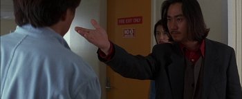 Movie still from “First Strike” (1996), directed by Stanley Tong – A man in a suit is holding his hand out to another man in a suit; Close Up shot, Over the shoulder angle