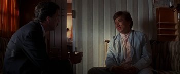 Movie still from “First Strike” (1996), directed by Stanley Tong – Two men are sitting in a chair and one of them is holding a cup; Medium shot, Over the shoulder angle