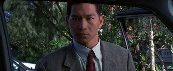 Movie still from “First Strike” (1996), directed by Stanley Tong – A person wearing a suit and tie; Close Up shot, Over the shoulder angle