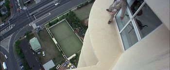 Movie still from “First Strike” (1996), directed by Stanley Tong – A man standing on the side of a building next to a tennis court; Extreme Wide shot, Overhead angle