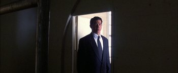 Movie still from “First Strike” (1996), directed by Stanley Tong – A man wearing a suit and tie standing in a doorway; Medium shot, Low angle