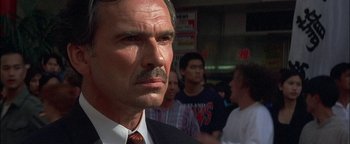 Movie still from “First Strike” (1996), directed by Stanley Tong – A person wearing a suit and tie; Close Up shot, Low angle