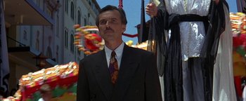 Movie still from “First Strike” (1996), directed by Stanley Tong – A man in a suit and tie standing in front of a carnival; Close Up shot, Low angle