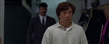 Movie still from “First Strike” (1996), directed by Stanley Tong – A man standing next to another man in a suit; Close Up shot, Over the shoulder angle