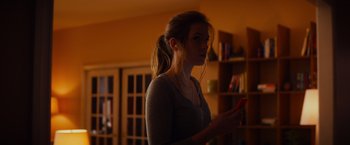 Movie still from “Poltergeist” (2015), directed by Gil Kenan – A woman standing in a living room holding a cell phone; Medium shot, Over the shoulder angle