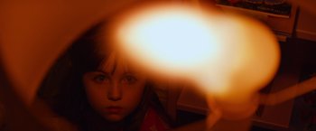 Movie still from “Poltergeist” (2015), directed by Gil Kenan – A young girl is looking at the camera with a light shining on her face; Extreme Close Up shot, High angle