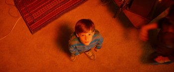 Movie still from “Poltergeist” (2015), directed by Gil Kenan – A boy sitting on the floor looking up at the camera; Medium shot, Overhead angle