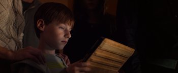 Movie still from “Poltergeist” (2015), directed by Gil Kenan – A young boy is looking at a book in a dark room; Close Up shot, Low angle