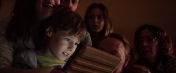 Movie still from “Poltergeist” (2015), directed by Gil Kenan – A young boy looking at a book with a group of people behind him; Close Up shot, High angle