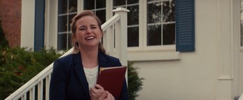Movie still from “Poltergeist” (2015), directed by Gil Kenan – A woman holding a book and smiling for the camera; Medium shot, Over the shoulder angle