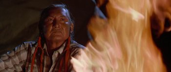 Movie still from “Poltergeist II: The Other Side” (1986), directed by Brian Gibson – An older man with long black hair wearing a white shirt and a red scarf; Close Up shot, Over the shoulder angle