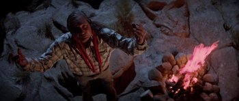 Movie still from “Poltergeist II: The Other Side” (1986), directed by Brian Gibson – A man standing in front of a fire in a cave; Medium shot, Overhead angle