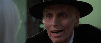 Movie still from “Poltergeist II: The Other Side” (1986), directed by Brian Gibson – An old man wearing a black hat and a white shirt; Close Up shot, Low angle