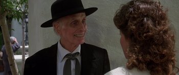 Movie still from “Poltergeist II: The Other Side” (1986), directed by Brian Gibson – An older man wearing a suit and a hat talking to an older woman; Close Up shot, Over the shoulder angle
