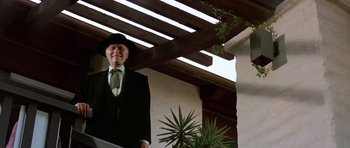 Movie still from “Poltergeist II: The Other Side” (1986), directed by Brian Gibson – An old man in a suit and a hat is standing outside; Medium shot, Low angle