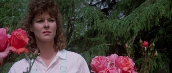 Movie still from “Poltergeist II: The Other Side” (1986), directed by Brian Gibson – A woman standing in front of a tree holding flowers; Close Up shot, Low angle