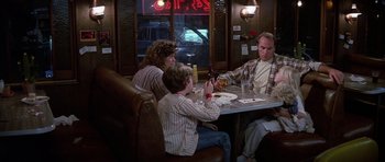 Movie still from “Poltergeist II: The Other Side” (1986), directed by Brian Gibson – Three people are sitting at a table in a restaurant; Medium shot, Over the shoulder angle